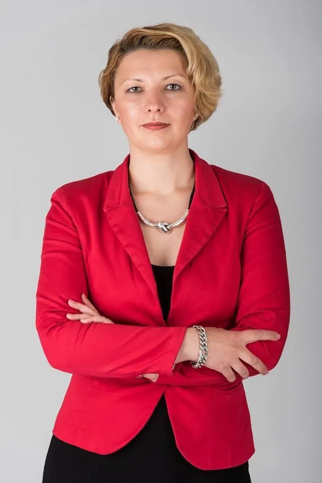 Laura Moiș, în sacou roșu, cu brațele încrucișate